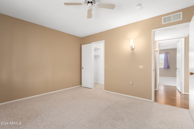 unfurnished bedroom featuring light carpet, a walk in closet, a textured ceiling, ceiling fan, and a closet