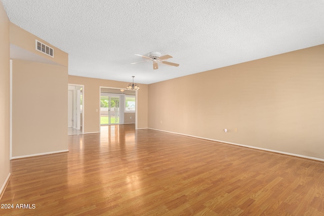 spare room featuring ceiling fan with notable chandelier, light wood-type flooring, and a textured ceiling