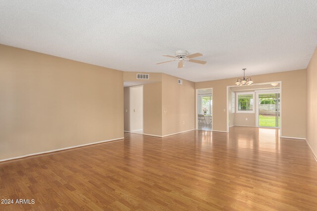 empty room with ceiling fan with notable chandelier, a textured ceiling, and light wood-type flooring