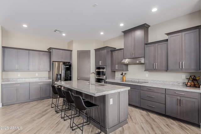 2516 W Joy Ranch Rd, Phoenix, AZ 85086 - kitchen featuring under cabinet range hood, stainless steel appliances, a sink, a kitchen breakfast bar, and light wood-style floors