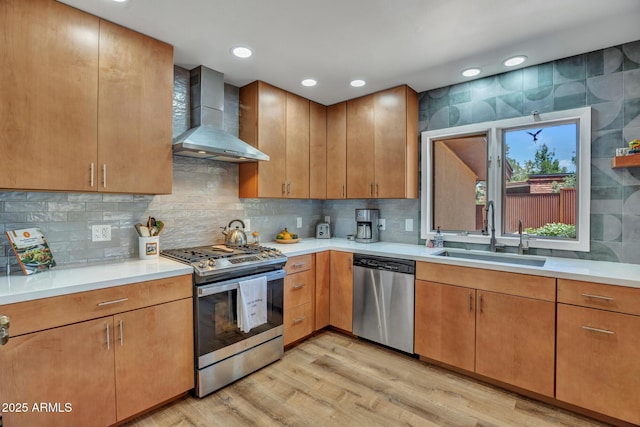 kitchen with appliances with stainless steel finishes, a sink, wall chimney range hood, light wood finished floors, and light countertops