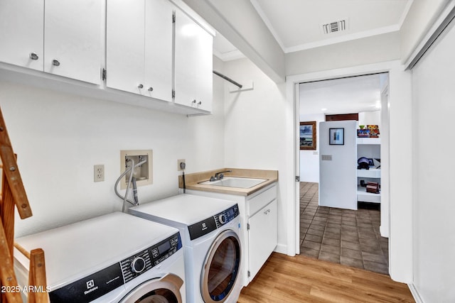 clothes washing area featuring washing machine and clothes dryer, cabinet space, ornamental molding, and light wood finished floors