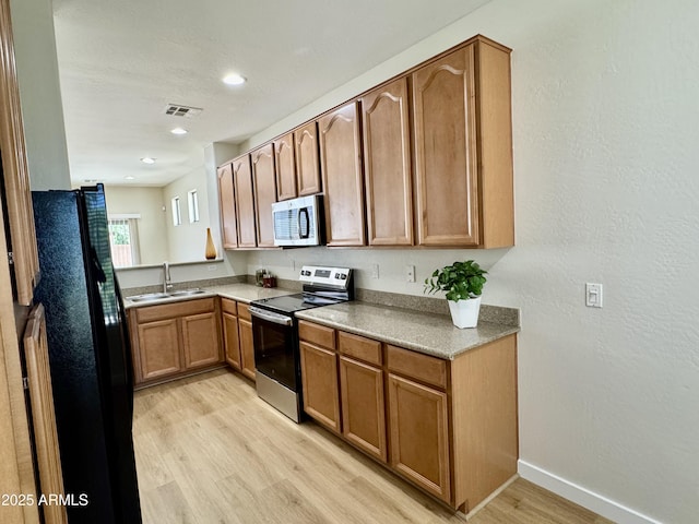 kitchen featuring a sink, appliances with stainless steel finishes, light wood-style floors, baseboards, and brown cabinetry