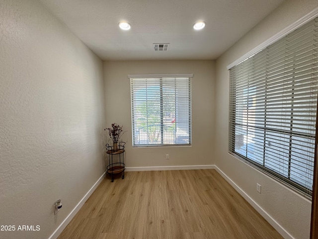 empty room with baseboards, visible vents, a healthy amount of sunlight, and light wood finished floors