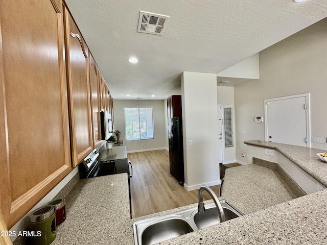 kitchen featuring light wood finished floors, a sink, brown cabinets, stainless steel appliances, and visible vents