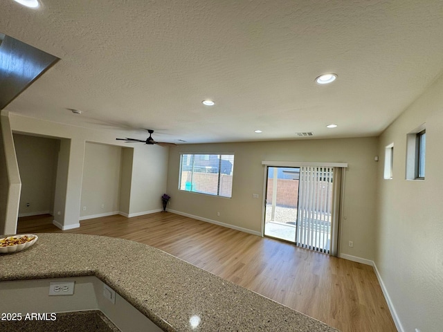 unfurnished living room with a textured ceiling, visible vents, baseboards, light wood-type flooring, and a ceiling fan