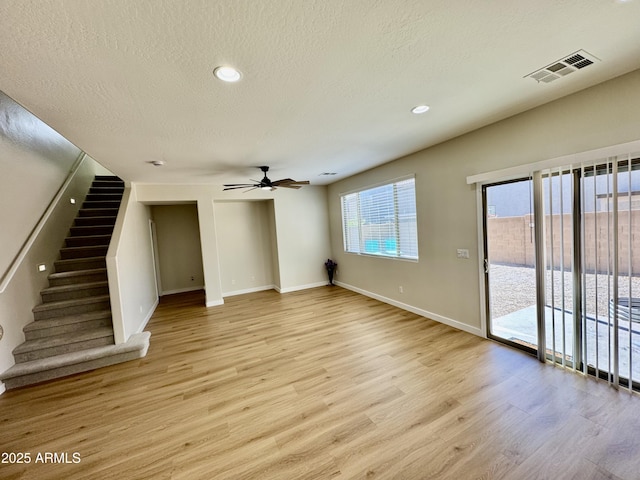 unfurnished living room featuring a ceiling fan, visible vents, light wood-style flooring, baseboards, and a textured ceiling