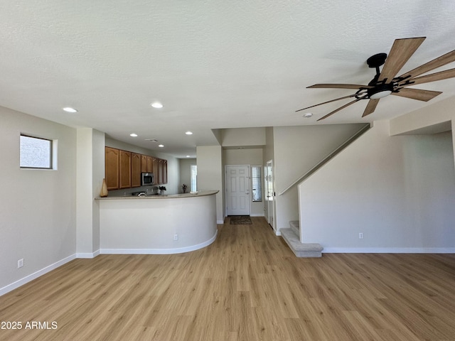 kitchen featuring stainless steel microwave, recessed lighting, light wood-style flooring, baseboards, and open floor plan