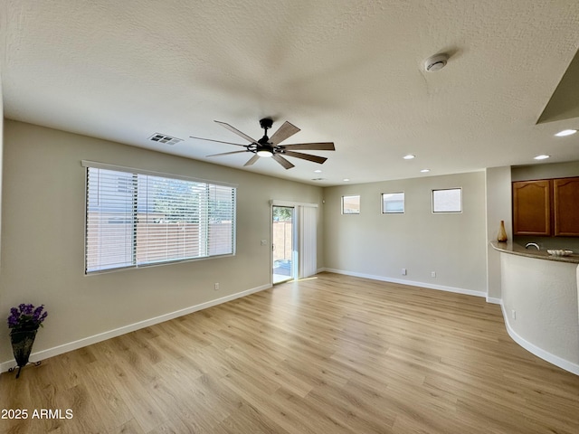 unfurnished living room with a textured ceiling, visible vents, recessed lighting, light wood finished floors, and a ceiling fan