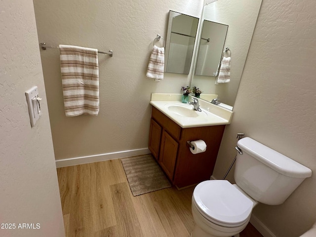 half bathroom with toilet, vanity, wood finished floors, and baseboards