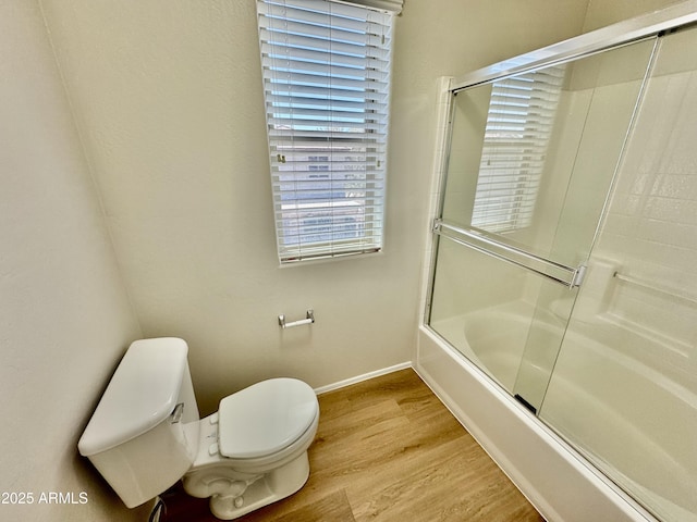 full bathroom with baseboards, wood finished floors, bath / shower combo with glass door, and toilet