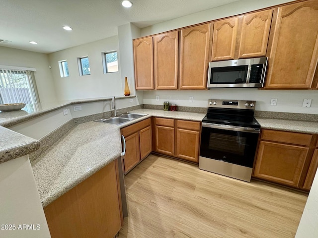 kitchen with light wood finished floors, recessed lighting, a sink, a peninsula, and appliances with stainless steel finishes