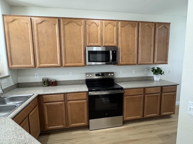 kitchen with light wood-style flooring, a sink, appliances with stainless steel finishes, and light countertops