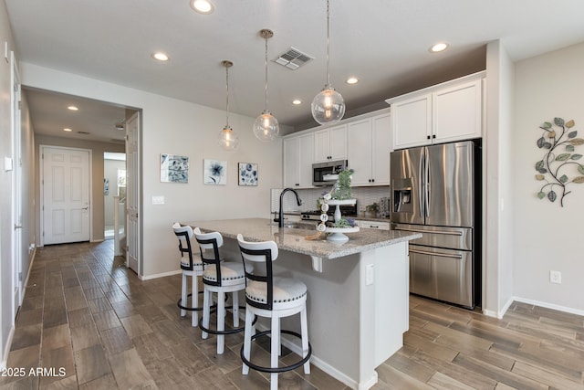 kitchen with white cabinetry, hanging light fixtures, an island with sink, and appliances with stainless steel finishes