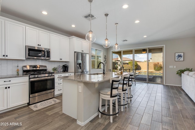 kitchen featuring white cabinetry, decorative light fixtures, stainless steel appliances, and an island with sink