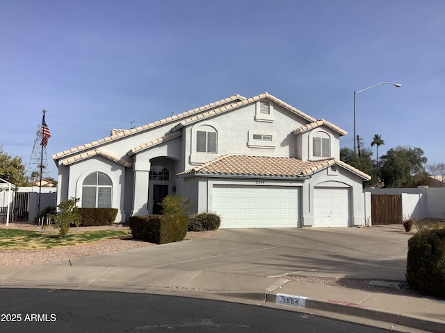 mediterranean / spanish-style home featuring a tiled roof, fence, driveway, and stucco siding