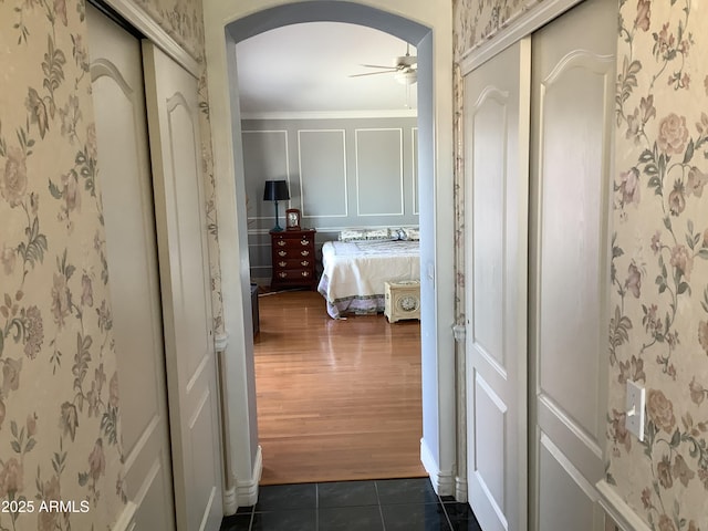 corridor with arched walkways, dark tile patterned flooring, and wallpapered walls