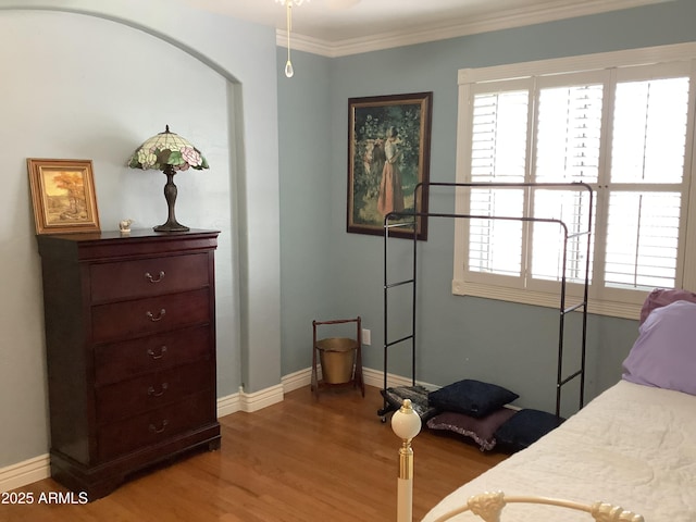 bedroom featuring ornamental molding, multiple windows, baseboards, and wood finished floors