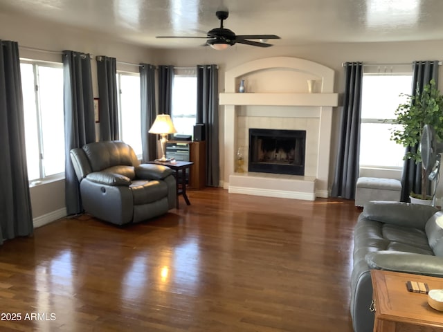 living room featuring a tiled fireplace, dark wood-type flooring, and a wealth of natural light