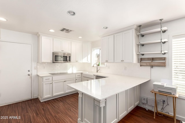 kitchen with a peninsula, visible vents, white cabinetry, light countertops, and stainless steel microwave