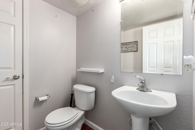 half bathroom with a textured wall, baseboards, a sink, and toilet