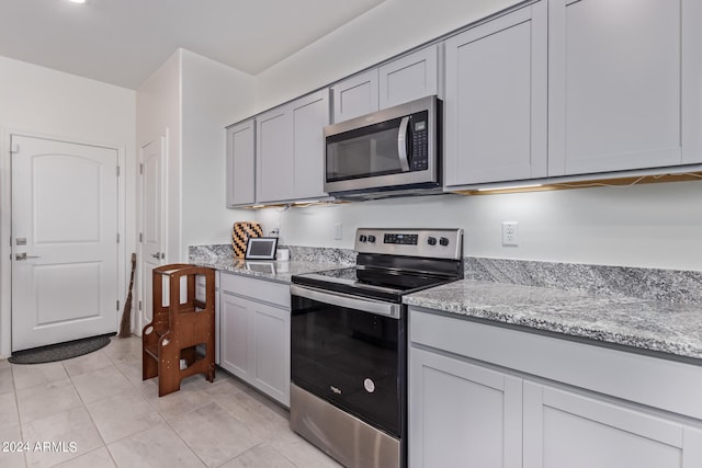 kitchen featuring gray cabinets, stainless steel appliances, light stone counters, and light tile patterned floors