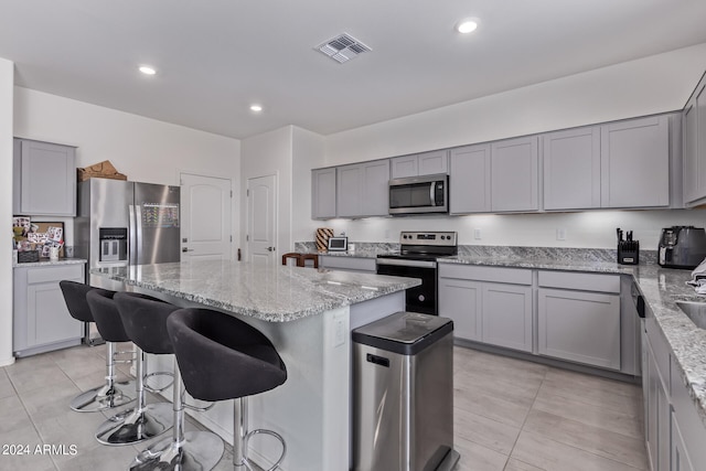 kitchen featuring a breakfast bar, light stone counters, a center island, light tile patterned flooring, and stainless steel appliances