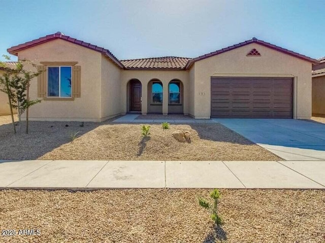 mediterranean / spanish house with a tiled roof, a garage, driveway, and stucco siding