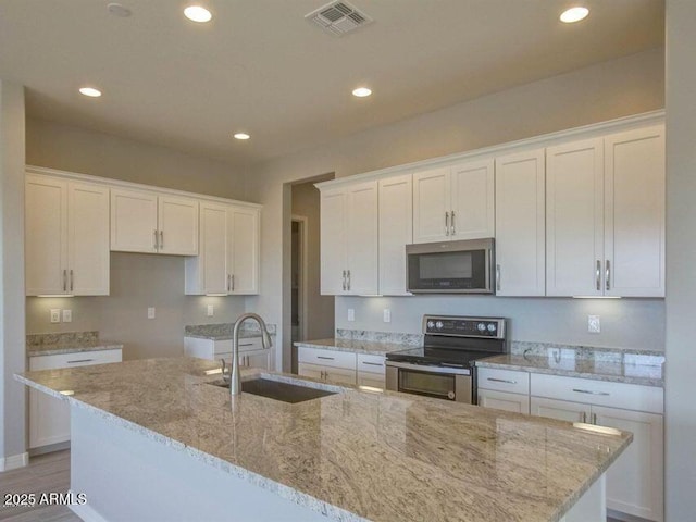 kitchen with a center island with sink, visible vents, a sink, stainless steel appliances, and white cabinetry