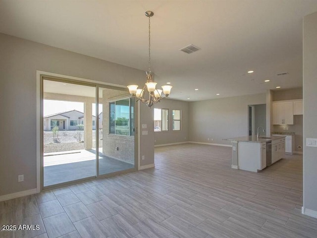 empty room with visible vents, baseboards, light wood-type flooring, a notable chandelier, and a sink