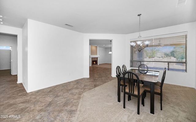 dining area featuring visible vents, baseboards, a notable chandelier, and a warm lit fireplace