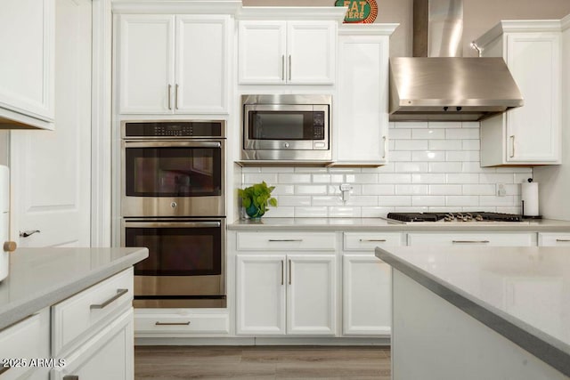 kitchen featuring stainless steel appliances, white cabinetry, and wall chimney range hood