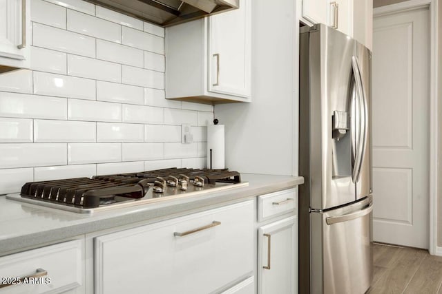 kitchen featuring tasteful backsplash, light hardwood / wood-style floors, white cabinetry, light stone countertops, and stainless steel appliances