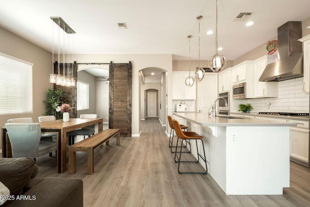 kitchen with hanging light fixtures, wall chimney exhaust hood, stainless steel appliances, and a barn door