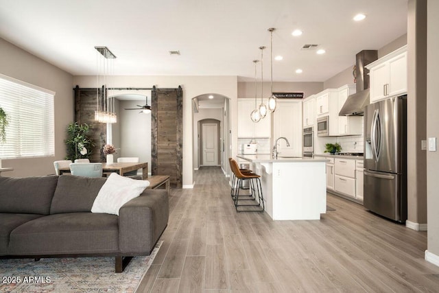 living room featuring ceiling fan, sink, a barn door, and light wood-type flooring