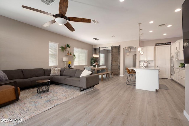 living room with ceiling fan, sink, light hardwood / wood-style flooring, and a barn door