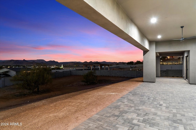 yard at dusk featuring a mountain view, ceiling fan, and a patio area