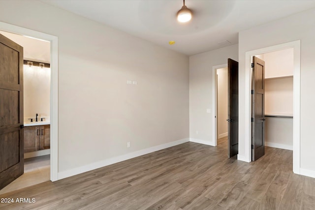 unfurnished bedroom with a closet, ensuite bathroom, hardwood / wood-style floors, and a spacious closet