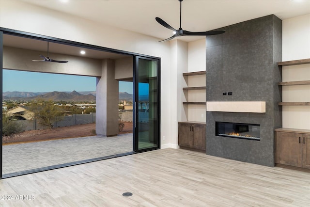 unfurnished living room with a mountain view, light hardwood / wood-style floors, ceiling fan, and a tiled fireplace