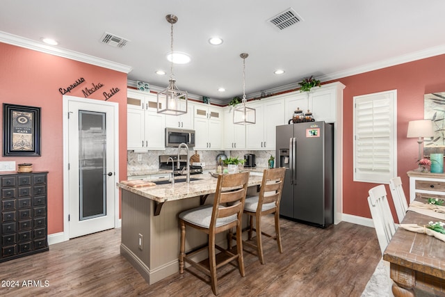 kitchen featuring crown molding, appliances with stainless steel finishes, a kitchen island with sink, hanging light fixtures, and white cabinetry