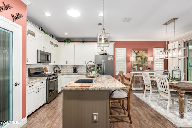 kitchen featuring sink, a center island with sink, stainless steel appliances, a kitchen bar, and decorative light fixtures