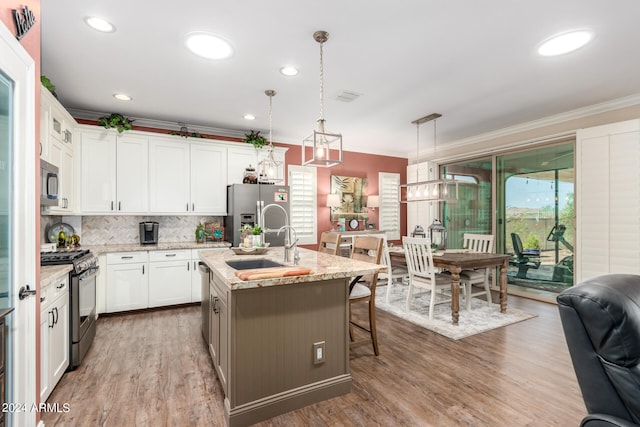 kitchen with pendant lighting, stainless steel appliances, light stone countertops, white cabinets, and a center island with sink