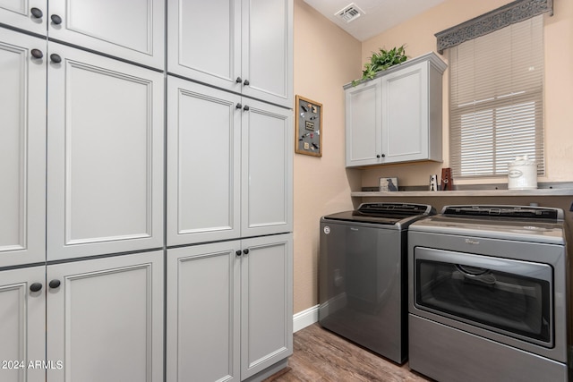 clothes washing area with washing machine and dryer, cabinets, and light wood-type flooring