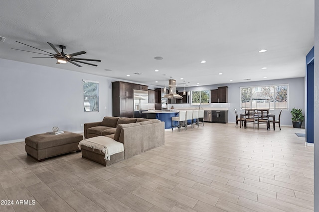 living room with ceiling fan, light hardwood / wood-style flooring, and a textured ceiling