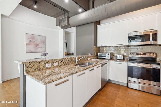 kitchen featuring a sink, appliances with stainless steel finishes, decorative backsplash, and a peninsula