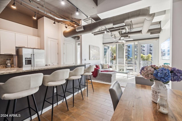 kitchen featuring light stone countertops, a high ceiling, rail lighting, white cabinetry, and stainless steel refrigerator with ice dispenser