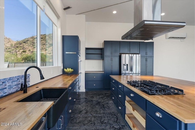 kitchen with stainless steel refrigerator with ice dispenser, island range hood, blue cabinets, wooden counters, and black gas cooktop