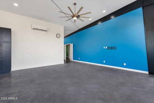 spare room featuring a wall mounted AC, finished concrete flooring, baseboards, ceiling fan, and a towering ceiling