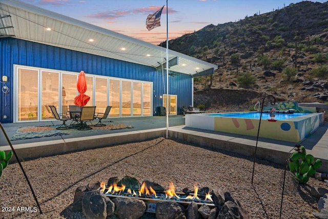 exterior space featuring a fire pit, board and batten siding, a patio, an outdoor pool, and a mountain view