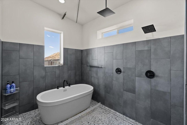 full bath with a freestanding tub, a tile shower, tile walls, and a healthy amount of sunlight